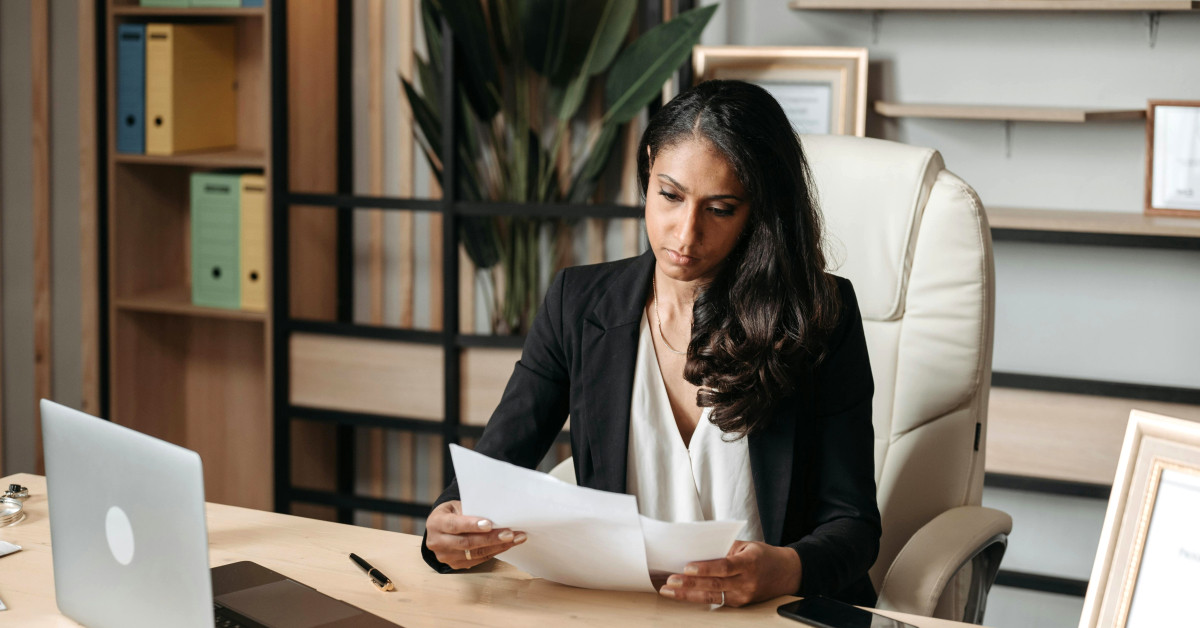Vrouw kijkt aandachtig naar papierwerk achter haar bureau